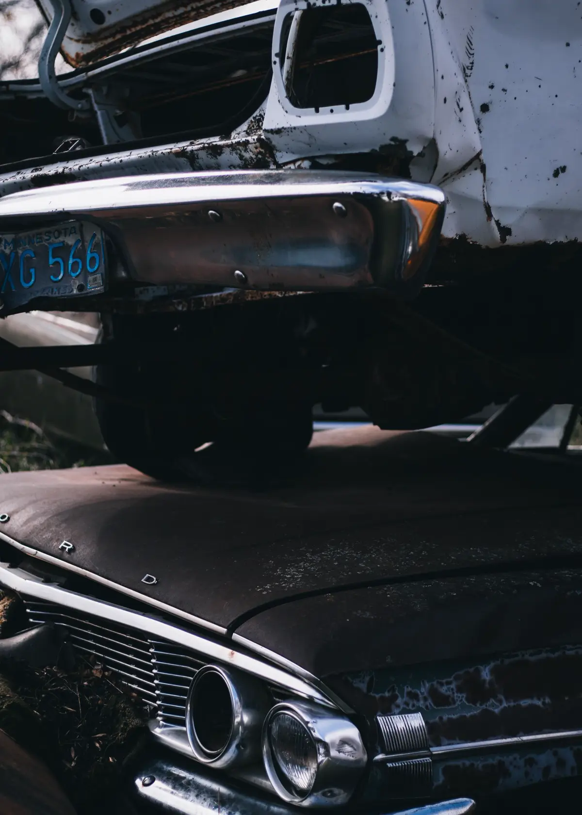 Stacked classic cars at a junk yard, chrome grille of an old Ford in the foreground