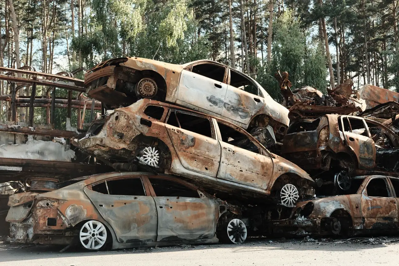 Pile of rusted junk cars at the edge of a wooded lot